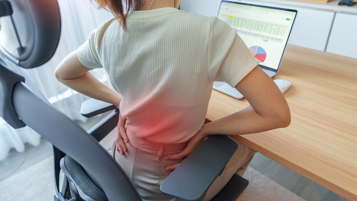 Mulher que tem dor nas costas durante o trabalho devido falta de ergonomia