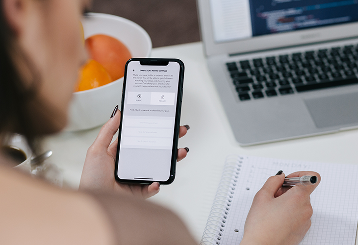 Mulher mexe no celular enquanto escreve em caderno