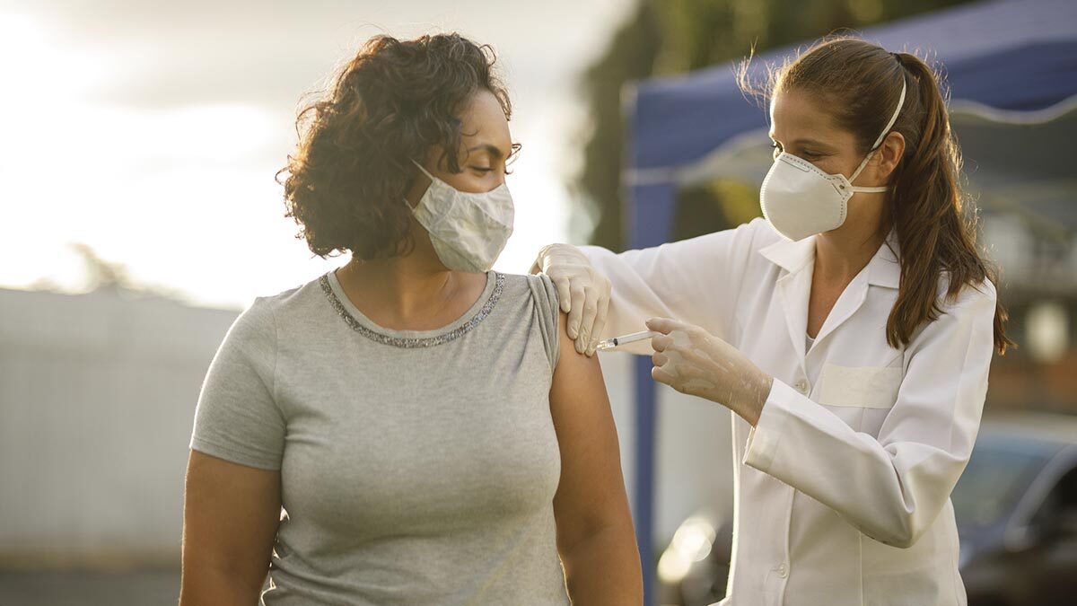 Mulher sendo vacinada e usando máscara