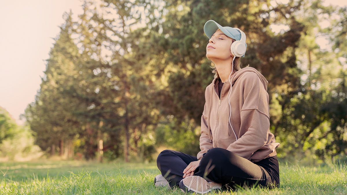 Mulher sentada no parque ouvindo musica e meditando