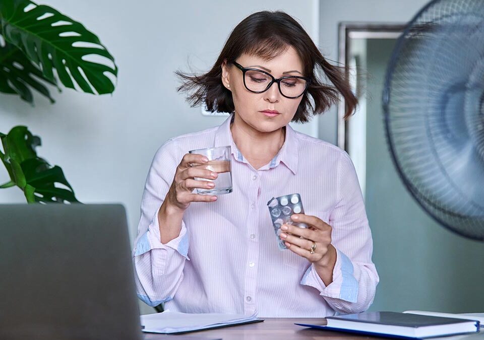 Mulher se medicando e com muito calor devido sintomas menopausa