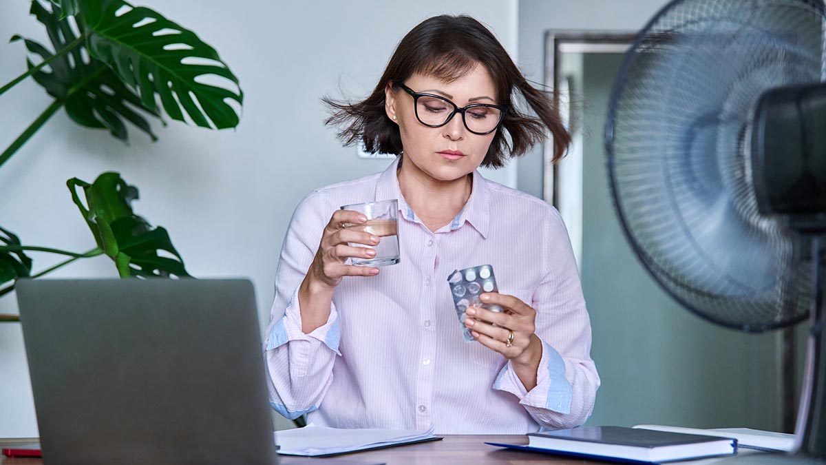 Mulher se medicando e com muito calor devido sintomas menopausa