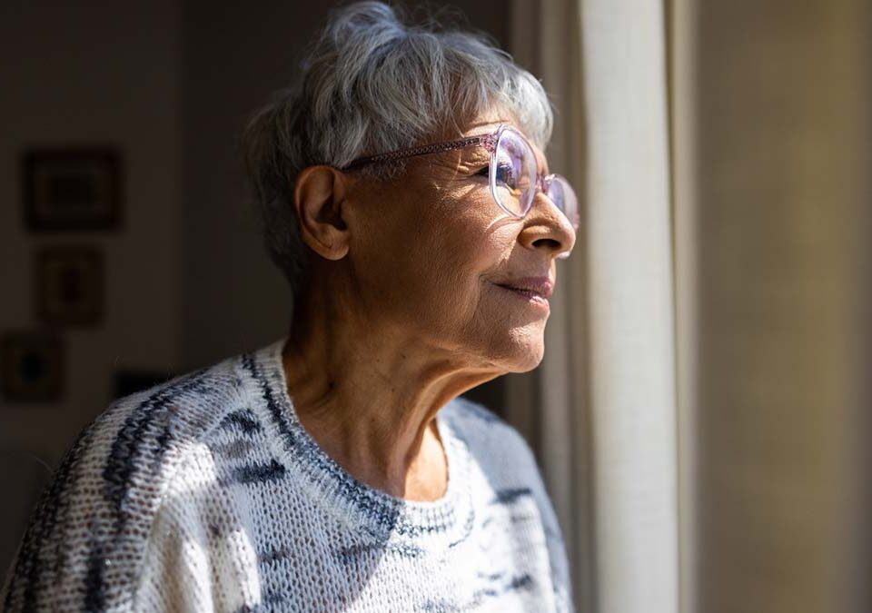 Idosa com olhando pela janela com inicio de Alzheimer