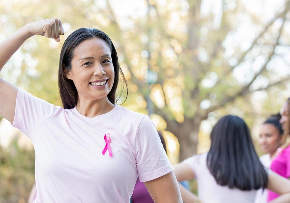Mulher com sorriso no rosto com roupa rosa e laço da campanha