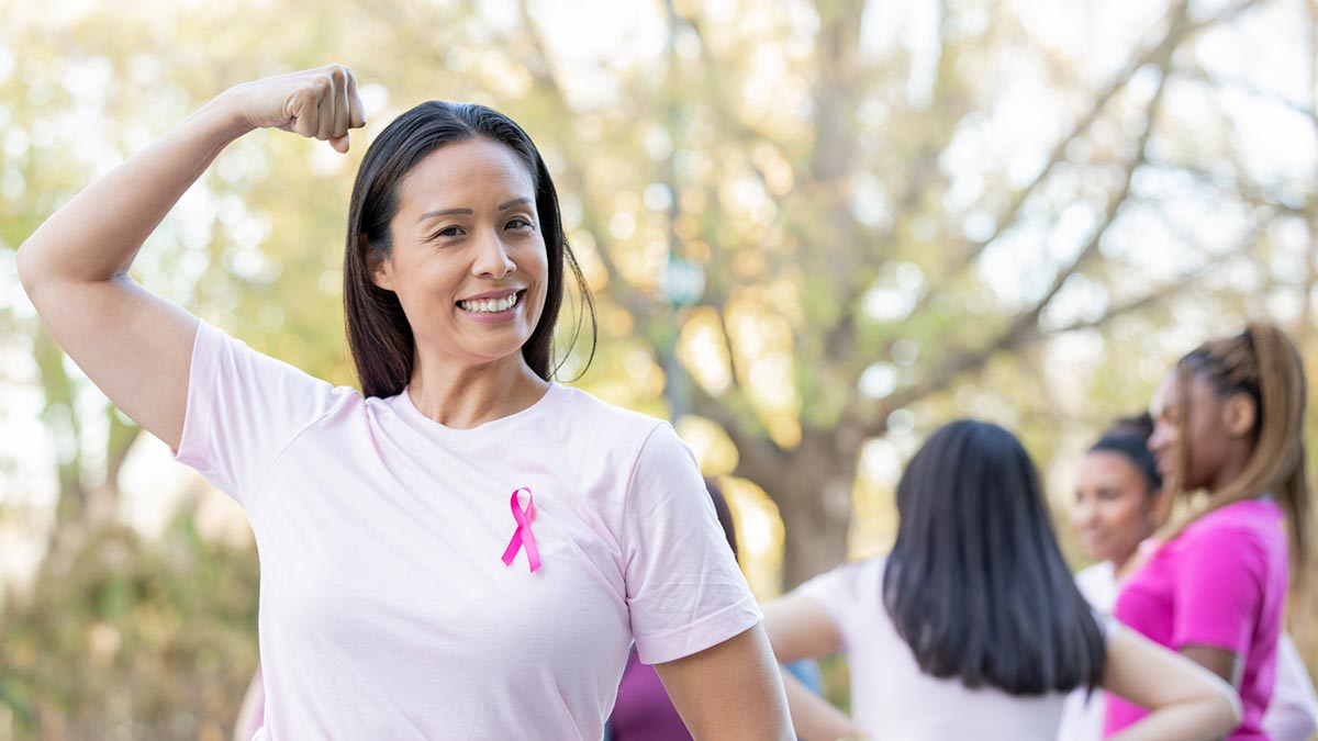 Mulher com sorriso no rosto com roupa rosa e laço da campanha