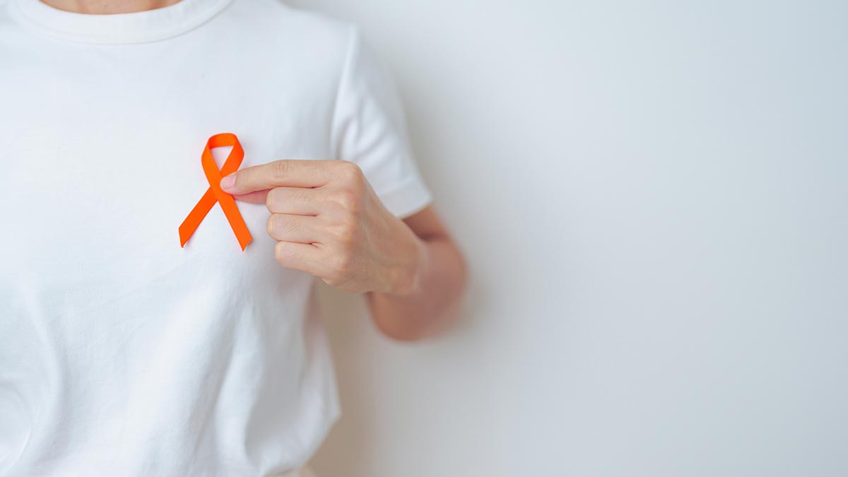Pessoa com camiseta branca e segurando laço laranja que representa o movimento Fevereiro Laranja